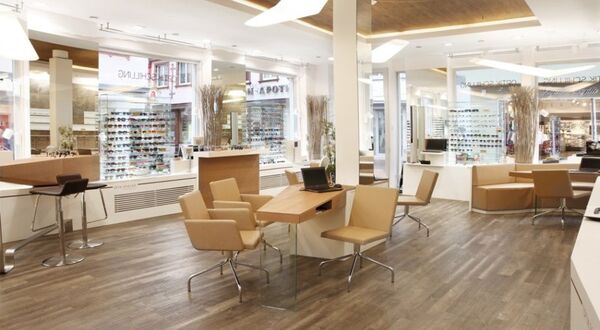 Modernes Optikergeschäft mit hellen Möbeln, großen Fenstern und vielfältiger Brillenauswahl.