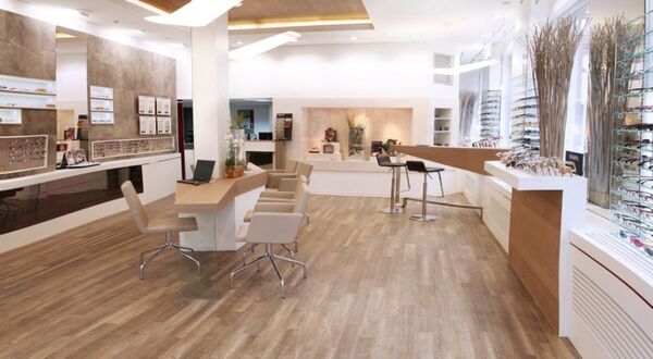 Modernes Optikerfachgeschäft mit Holzfußboden, Beratungstischen und Brillenauslage.